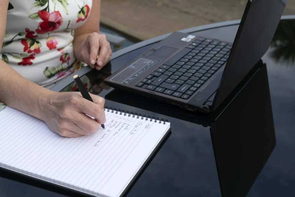 Person writing notes next to a laptop